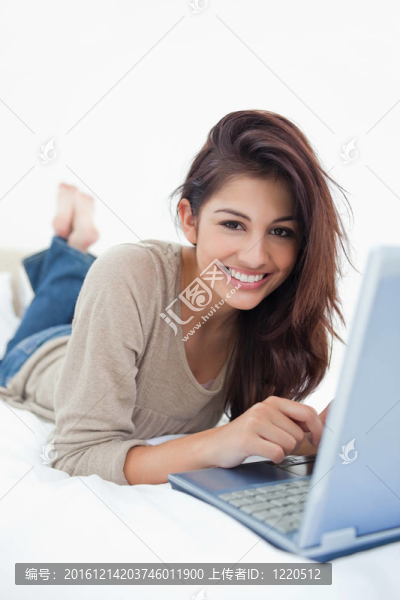一個面帶微笑的女人交叉著；躺在筆記本電腦前的床上。