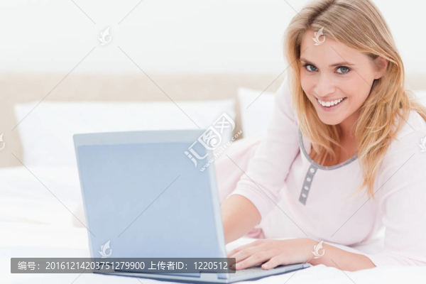 一個(gè)躺在床上的女人一邊微笑一邊看著筆記本電腦。