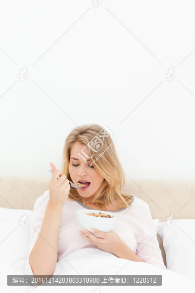 一個(gè)女人手里拿著一碗麥片的垂直鏡頭，她正要吃一勺麥片粥。