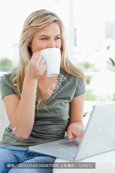 一個(gè)女人一邊看著一邊，一邊在筆記本上一邊喝著杯子里的飲料。