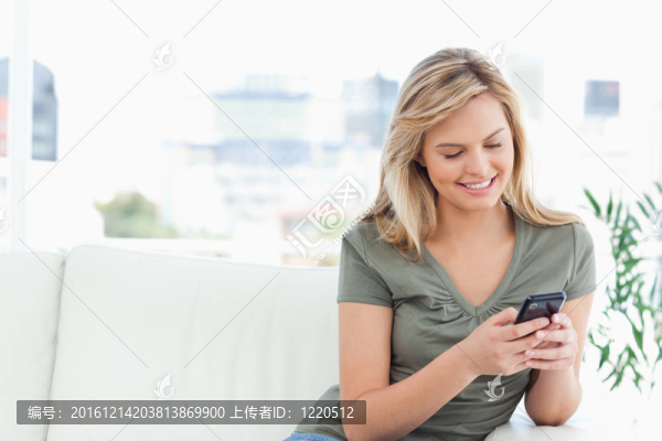 女人坐在沙發(fā)上，看著和使用她的手機和微笑