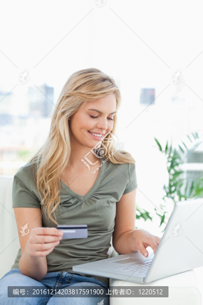 沙發(fā)上的女人；她拿著信用卡，用筆記本電腦微笑。