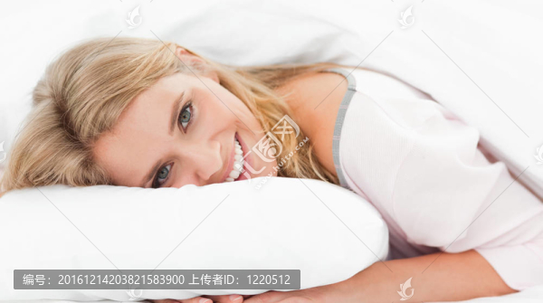 一個女人躺在床上，雙手枕在枕頭上，頭上戴著眼睛，微笑著。
