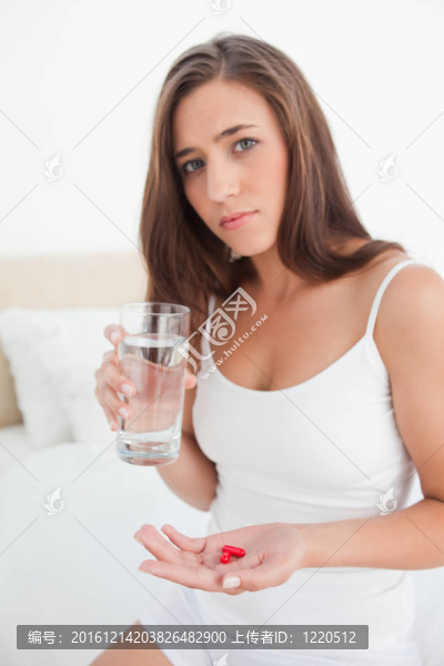 一個女人看上去很擔(dān)心，因為她正在決定用另一只手拿著一杯水吃藥。