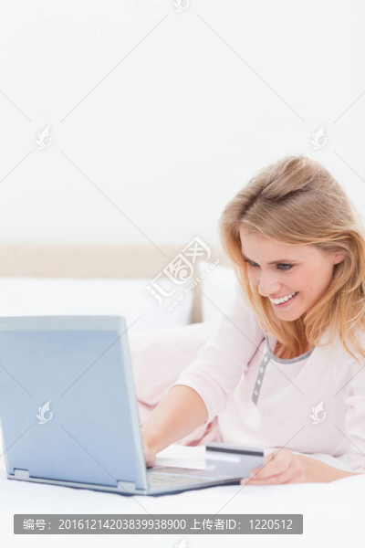 一個微笑的女人特寫鏡頭，看著她的筆記本電腦躺在床上。