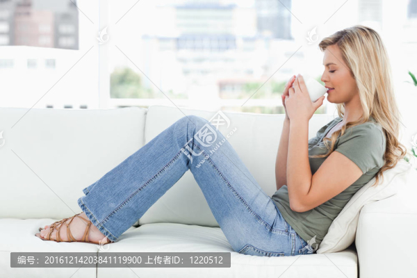 一個女人側(cè)身坐在沙發(fā)上；一個杯子舉到鼻子上；她的眼睛閉著。