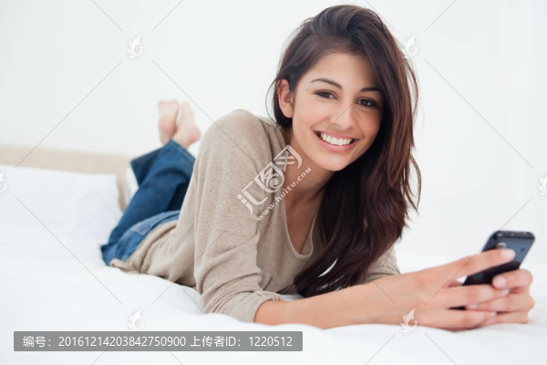 一個(gè)微笑的女人把她的手機(jī)放在她面前，因?yàn)樗诖采舷蚯翱础? title=