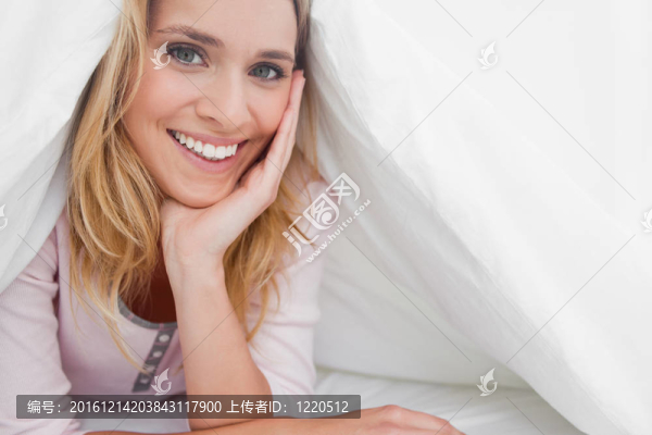 一個女人在被子下面，她的手支撐著她的頭，她微笑著向前看。