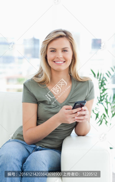 一個(gè)女人坐在沙發(fā)上的特寫鏡頭；她拿著手機(jī)微笑著。