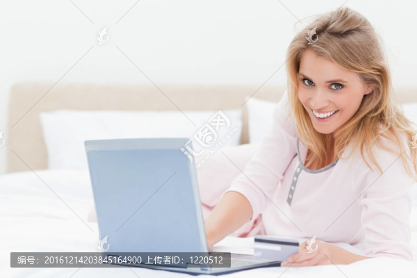 一個(gè)躺在床上的女人；她用筆記本電腦微笑著向前看。