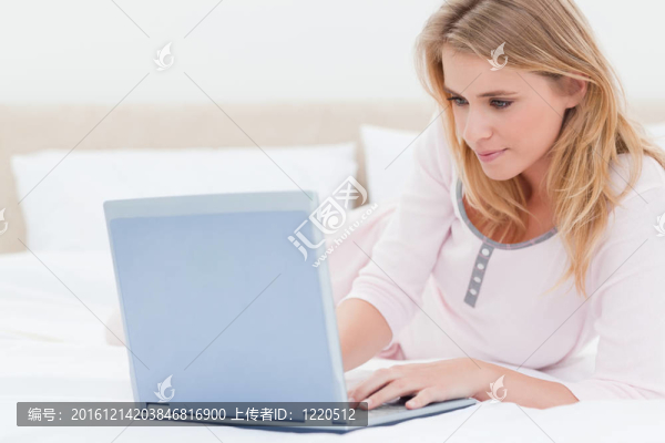 躺在床上的女人；同時(shí)使用筆記本電腦