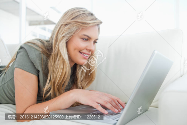 女人微笑著，當(dāng)她躺在沙發(fā)上使用筆記本電腦時(shí)