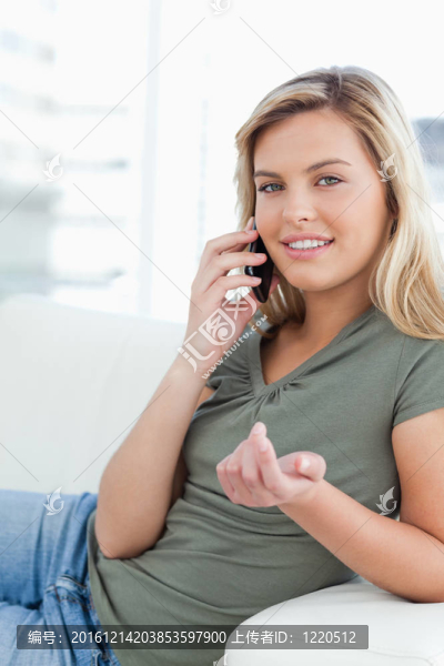 一個(gè)女人的手微微抬起，微笑著，一邊躺在沙發(fā)上一邊打電話。