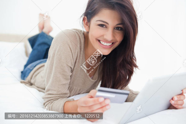 一個(gè)面帶微笑的女人拿著信用卡和平板電腦在她面前看著她。