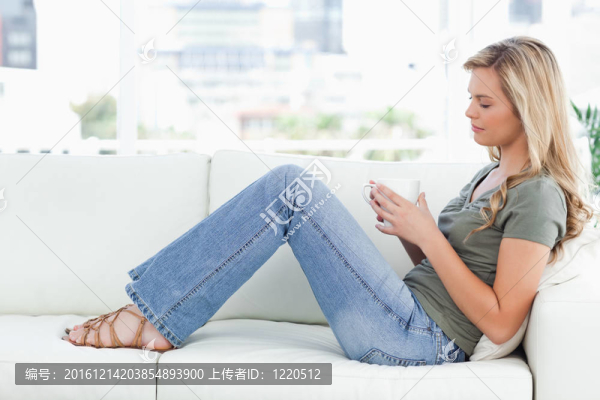 一個女人坐在沙發(fā)上，手里拿著杯子，眼睛閉著。