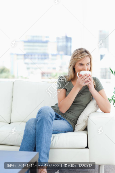 一個女人坐在沙發(fā)上，頭上戴著一個杯子，向旁邊望去。