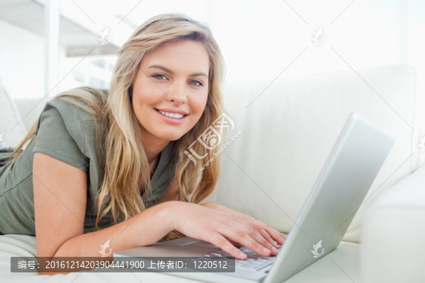 一個女人用筆記本電腦；在沙發(fā)上躺著時一直向前看。