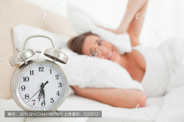 女人用枕頭捂住耳朵，因為鬧鐘響了
