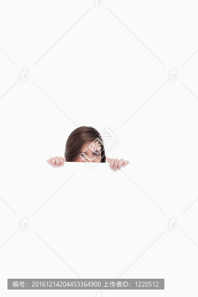 年輕女人躲在一張空白的海報(bào)后面，一邊眨著眼睛