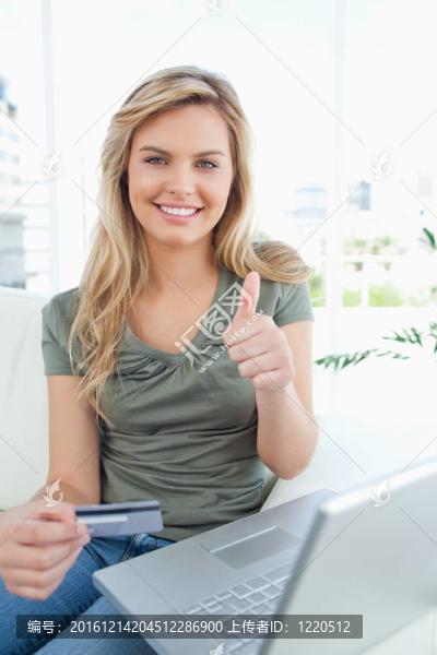 手里拿著信用卡的女人和她旁邊的筆記本電腦；微笑著豎起大拇指。
