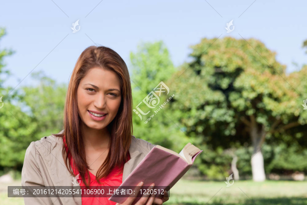 女人笑嘻嘻的看著在一個陽光明媚的草地面積在她手中一本書正前方
