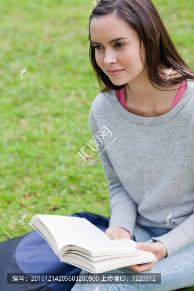 年輕的平靜的女孩拿著一本書在一個公共花園一邊看向一邊