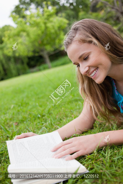 年輕女人微笑著躺在公園看書