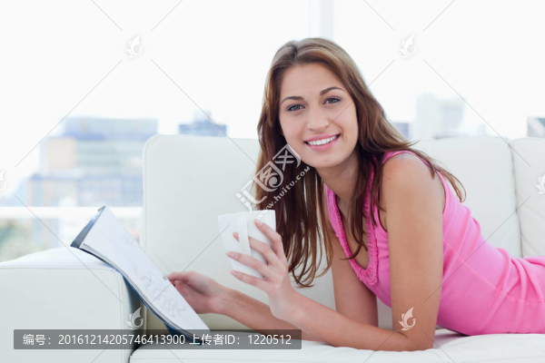 年輕的女人呈現(xiàn)出巨大的微笑而讀書和喝咖啡