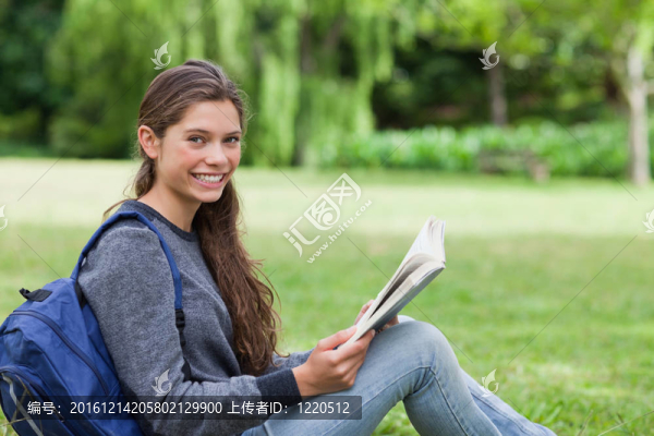 年輕的微笑女孩坐在草地上看書