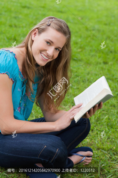 年輕女子微笑著看著相機(jī)一邊看書(shū)