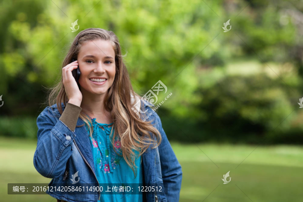 年輕的微笑女孩站在公園里打電話