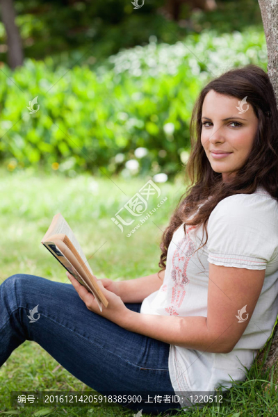 年輕輕松的女人一邊看著相機(jī)一邊拿著一本書