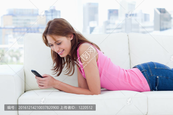 年輕女子躺在舒適的沙發(fā)上一邊發(fā)短信