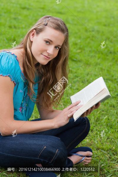 年輕輕松的女孩在公園的草地上盤腿坐著看書