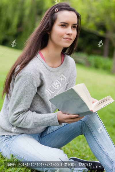 體貼的年輕女孩坐在草地上，手里拿著一本書