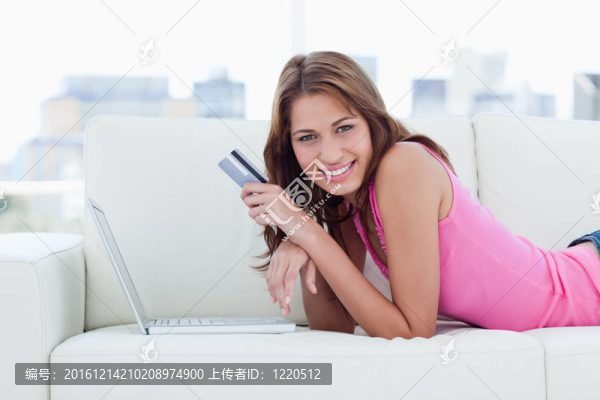 年輕女子躺在沙發(fā)上，手里拿著她的信用卡