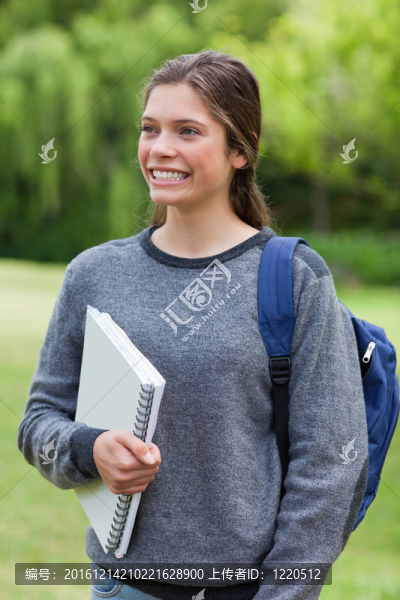 年輕女孩站著站著拿著筆記本，露出燦爛的笑容