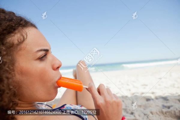海灘上的年輕漂亮的女人吃冰棒