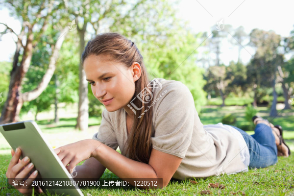 躺在草坪上的一個(gè)拿著平板電腦的婦女