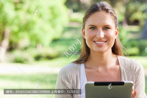 微笑的女子坐在草坪上用平板電腦