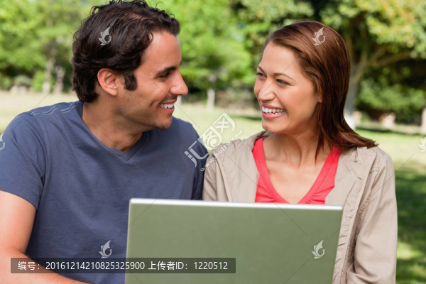 兩個朋友在陽光明媚的日子里在公園里抱著一張平板電腦，開心地微笑著看著對方
