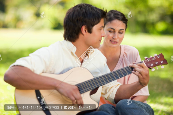 女人聽她的朋友彈吉他，因?yàn)樗麄兌甲诒舜伺赃叺牟莸厣? title=