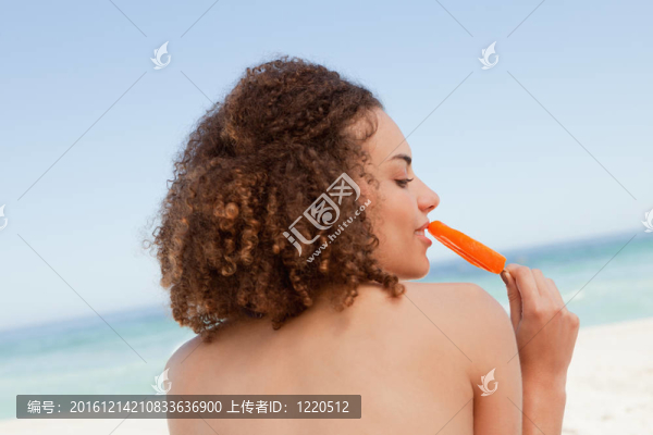 一個年輕漂亮的女人在大海面前吃橘子冰棍的背影