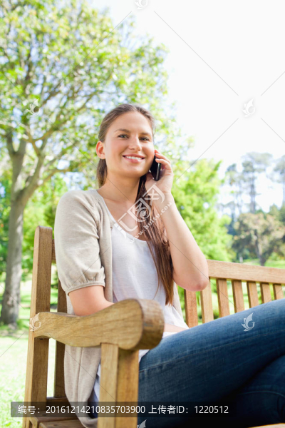 微笑的女人在公園長(zhǎng)椅上打電話