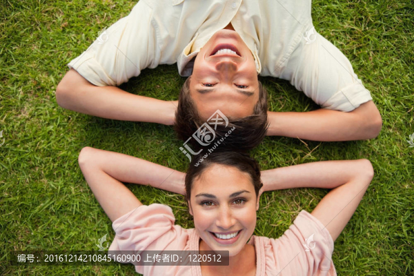 男人和女人微笑著，頭朝下躺著，兩只胳膊擱在草地的脖子后面