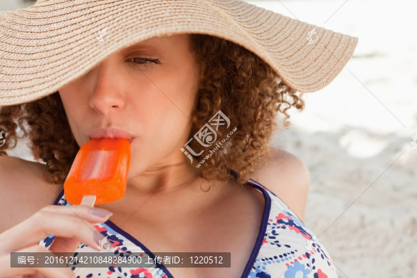 年輕漂亮的女人戴著草帽一邊吃著美味的雪糕