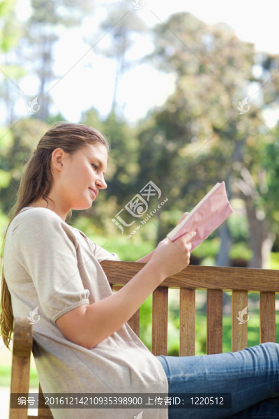 一個女人在公園長椅上看書的一面