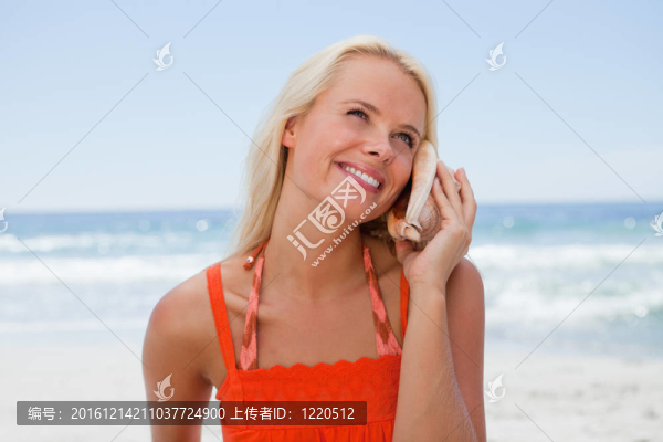 年輕的金發(fā)女人聽著大海的聲音，帶著貝殼微笑著