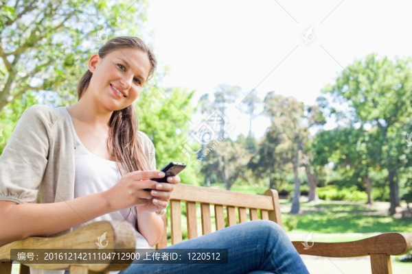 微笑的女人在公園長(zhǎng)椅上寫短信