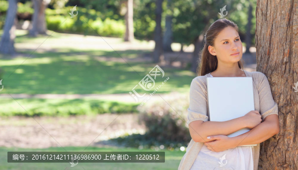 抱著筆記本電腦的女人靠在樹上